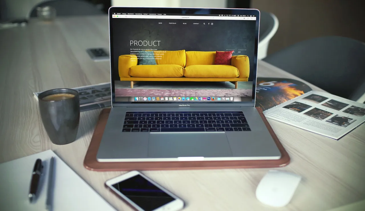 A laptop open on a desk showing a product page, beside a mug and a phone