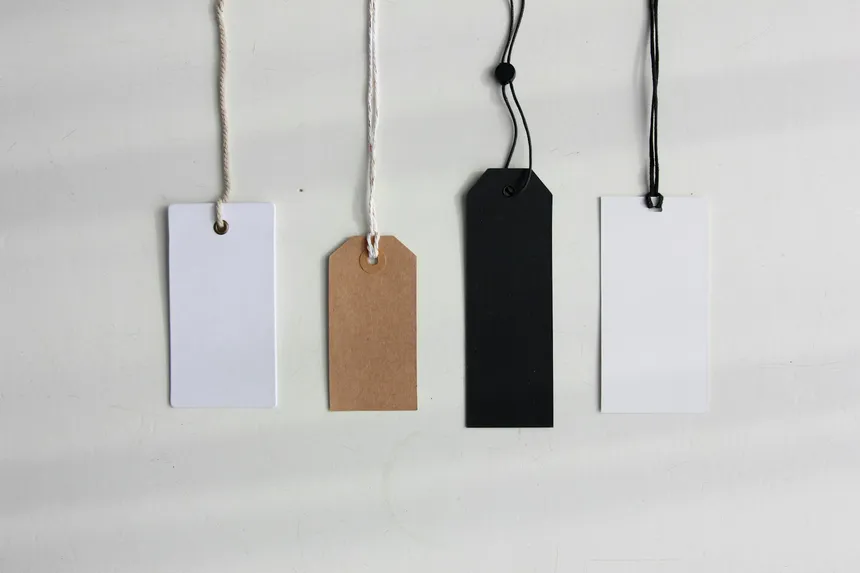 Four blank paper price tags hanging on strings against a pale background
