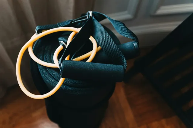 A resistance band and moulded handles coiled on a bench, load set by where you stand rather than by a number