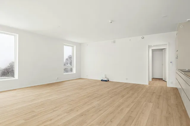 An empty rented room with pale walls and a bare wooden floor, lit by two windows