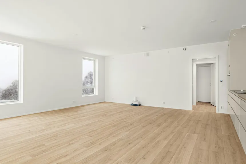 An empty rented room with pale walls and a bare wooden floor, lit by two windows