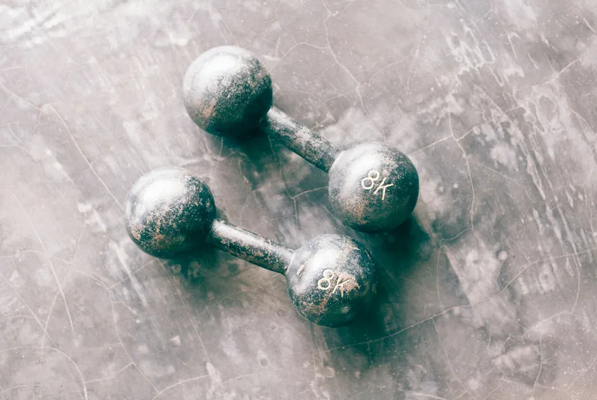 A pair of old dumbbells with the paint chipped away to bare metal, on a worn floor