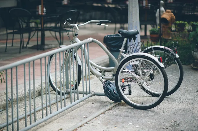 A three-wheeled trike parked at a railing, seen from behind so both rear wheels and the width between them are visible