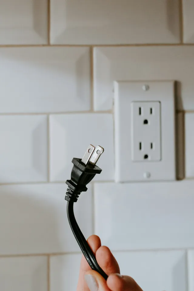 A power cord hanging unplugged beside a wall socket on a tiled wall