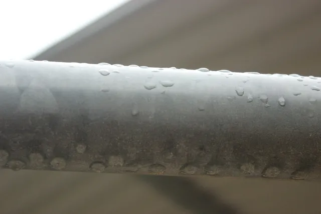 Water beaded across a cold metal pipe, the same condensation that forms on bare iron