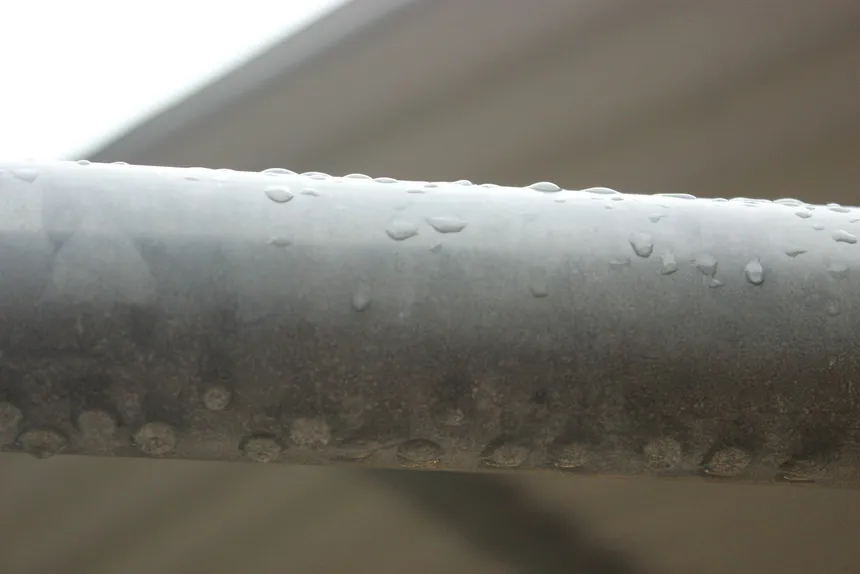 Water beaded across a cold metal pipe, the same condensation that forms on bare iron