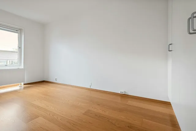 A bare rented room with white walls, a wooden floor and a single window
