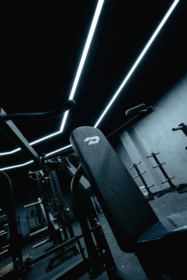 A dark gym interior with a rack and machines picked out by strip lighting