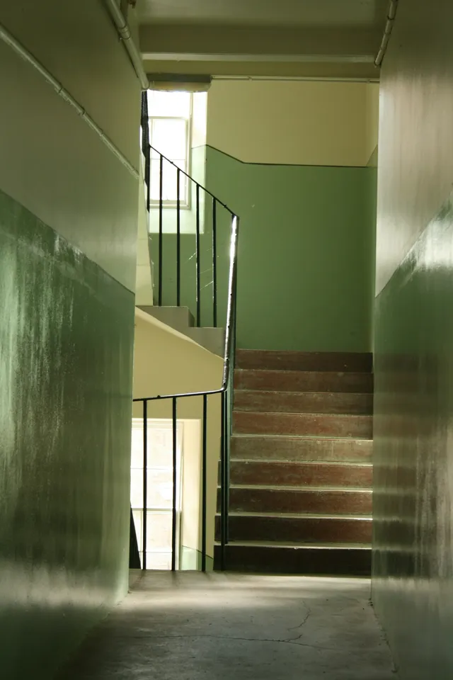 A stairwell photographed at the half-turn, one flight arriving at a landing and another leaving at right angles