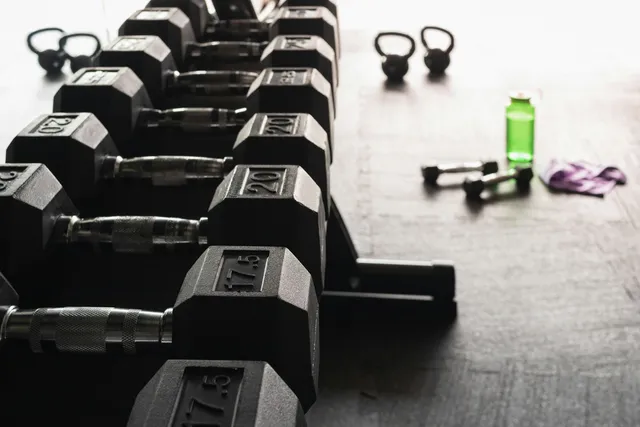 A rack of hex dumbbells in ascending weights beside a water bottle on a gym floor