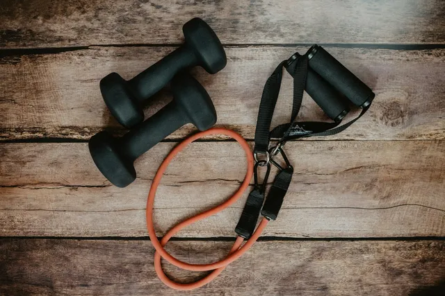 A resistance band with moulded handles coiled beside two small dumbbells on a wooden floor