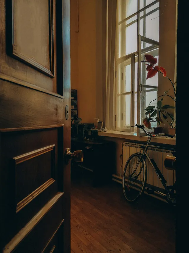 A bicycle parked in a dim room beside a tall window and a dark doorway