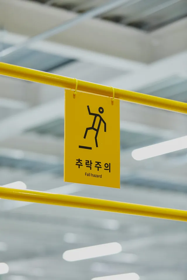 A yellow warning sign fixed to a metal handrail in a public building