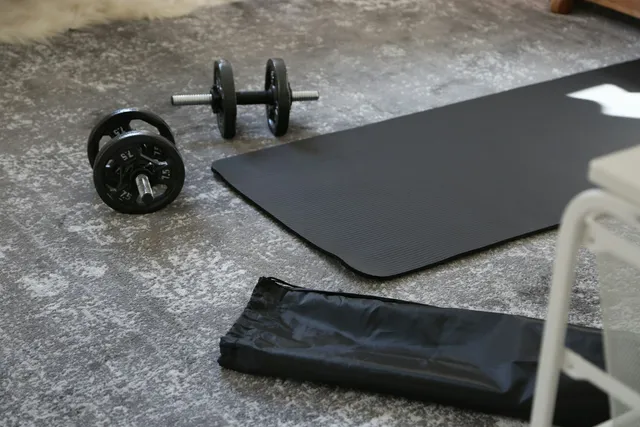 A thin exercise mat rolled out on a bare concrete floor with a dumbbell and a carry bag beside it