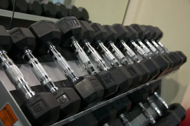 A commercial gym rack holding a full run of fixed hex dumbbells from light to heavy